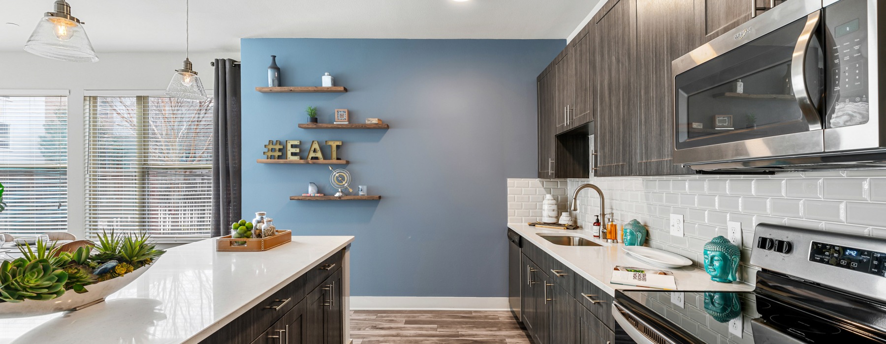 Modern apartment kitchen featuring stainless steel appliances, dark grey cabinetry, and a large kitchen island